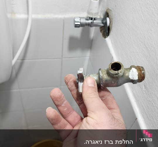 יד מחזיקה ברז ישן ליד צינור מים